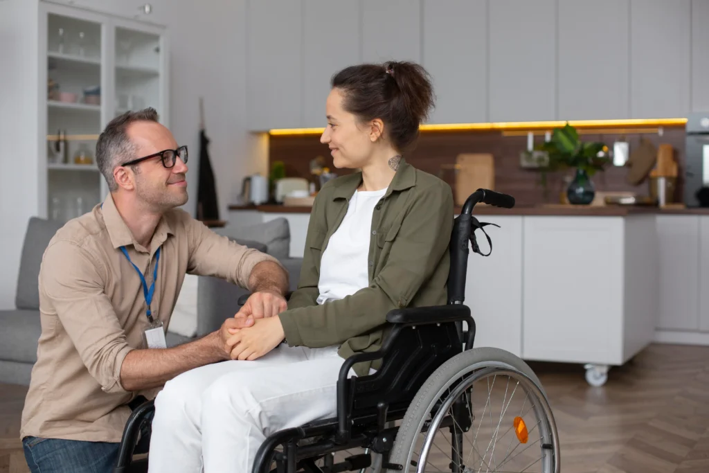 Woman in a wheelchair holding hands with a caregiver in a warm home environment.